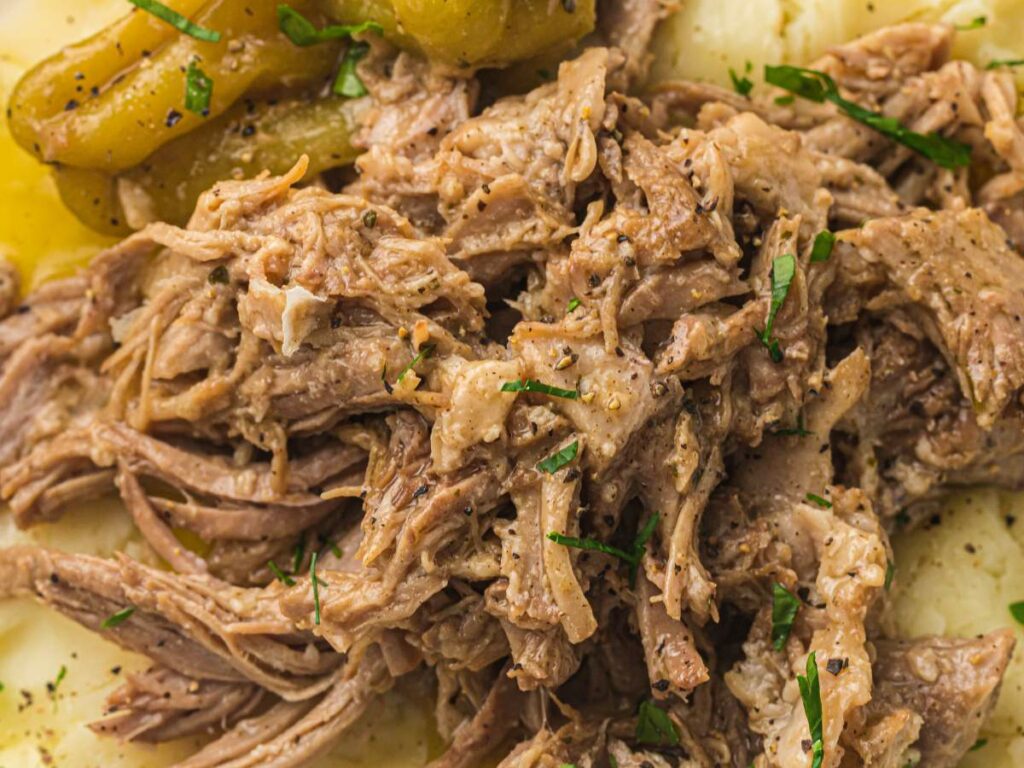 Shredded beef served over mashed potatoes, garnished with chopped herbs.