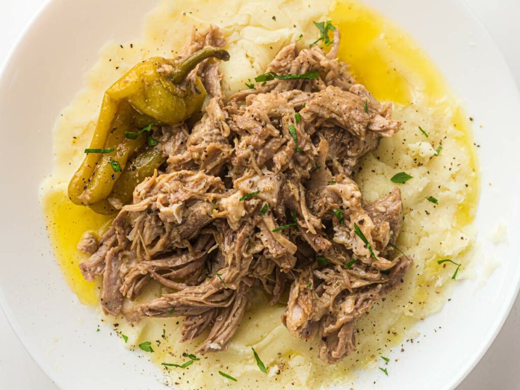 Shredded beef served over mashed potatoes, garnished with herbs and a whole pepperoncini.