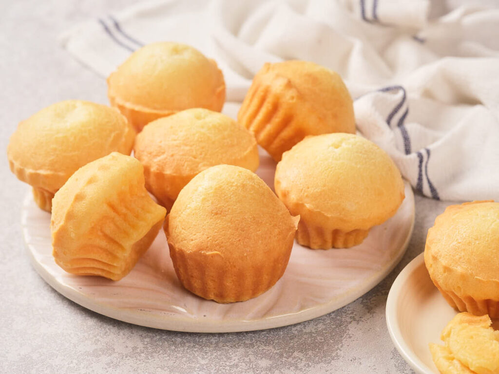 A plate of plain golden cupcakes, with a few more on a smaller plate.