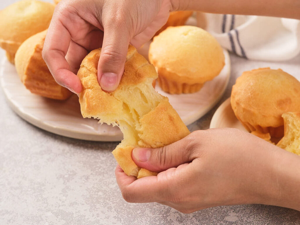 A person holding a piece of bread on a light surface.
