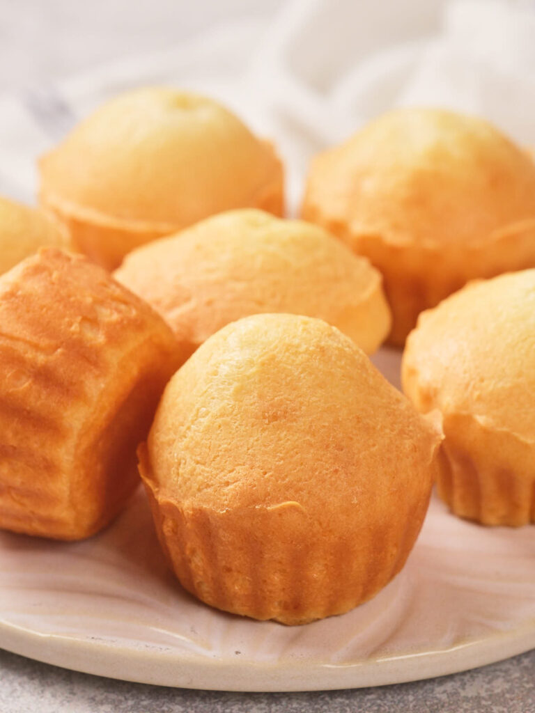 A plate with several plain, golden-brown cupcakes on a white plate.
