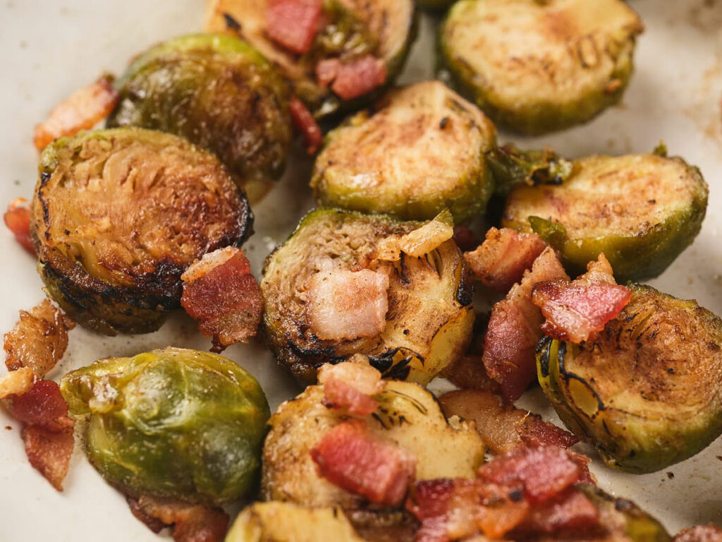 Roasted Brussels sprouts cut in half and cooked with crispy bacon pieces on a white plate.