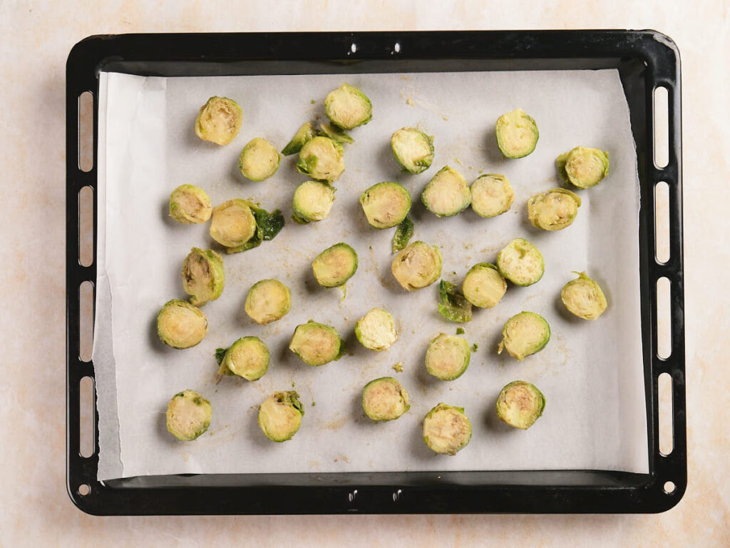 A baking tray lined with parchment paper holds halved Brussels sprouts spread out evenly.