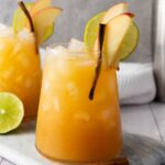 A glass of apple cider mocktail garnished with apple slices, lime wheel, and a cinnamon stick.