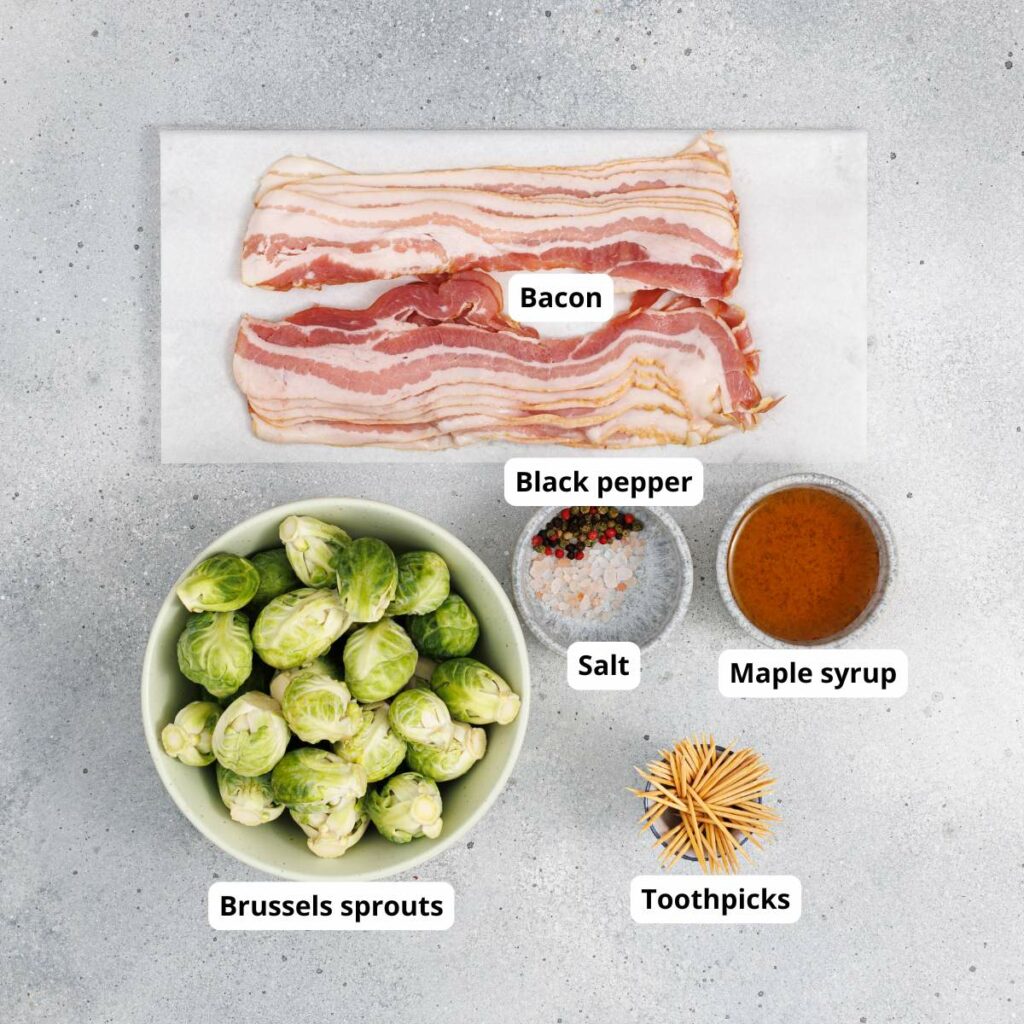 Bacon, Brussels sprouts, black pepper, salt, maple syrup, and toothpicks arranged on a gray surface, each labeled with text.