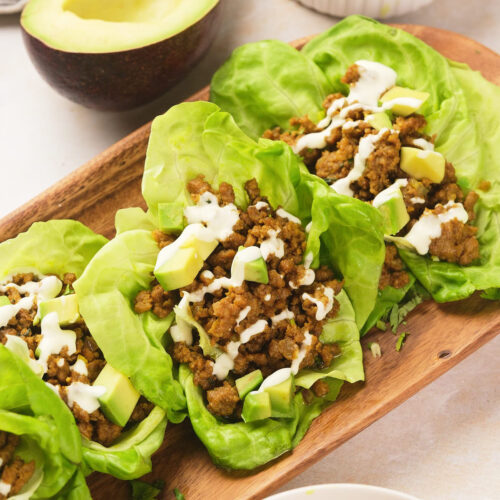 Three lettuce leaves filled with seasoned ground meat, diced avocado, and a drizzle of white sauce.