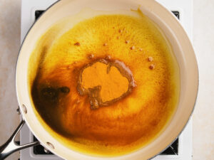 A saucepan on a stovetop containing melted butter and turmeric, with the spices beginning to mix and bubble.