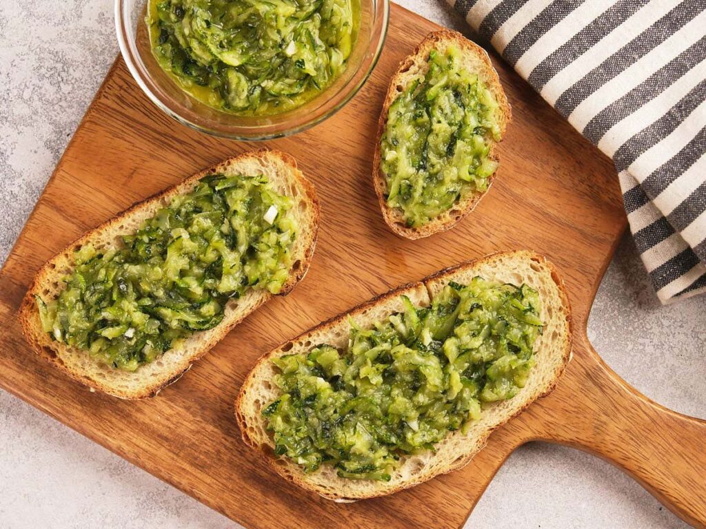 Three slices of bread topped with green zucchini spread on a wooden board.