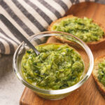 A small glass bowl of grated zucchini with butter and herbs, placed on a wooden board.