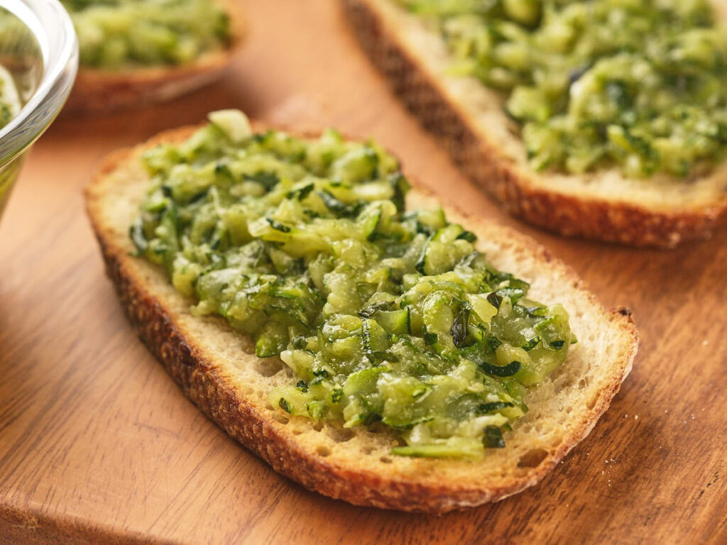 A slice of bread topped with a green vegetable spread, placed on a wooden surface.