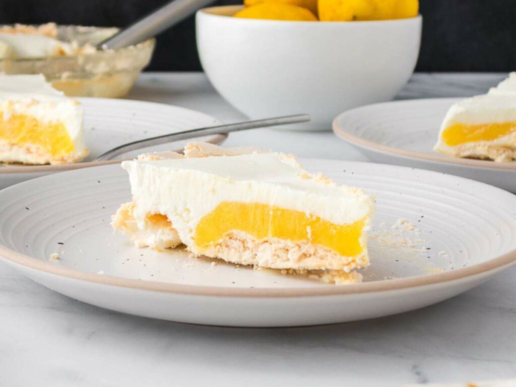 A slice of lemon angel pie with a creamy topping and yellow filling sits on a white plate.