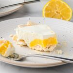 A slice of lemon dessert with a creamy layer and crumbly crust on a white plate.