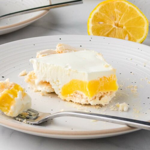 A slice of lemon dessert with a creamy layer and crumbly crust on a white plate.