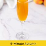 A champagne flute filled with orange mimosa sits on a white marble surface.