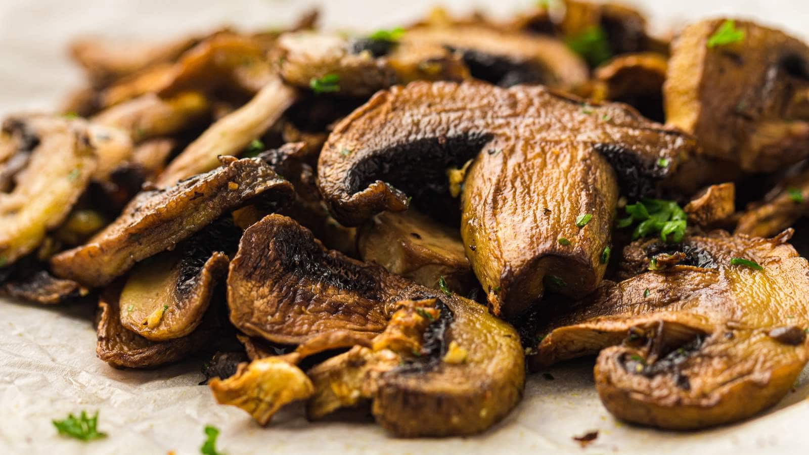 Close-up of sliced, cooked mushrooms garnished with small pieces of fresh herbs on a light-colored surface.