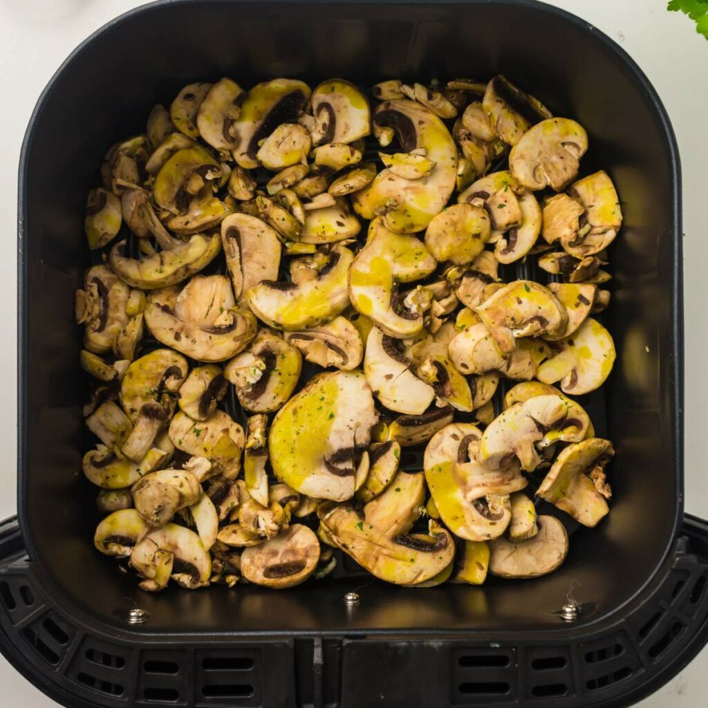 Sliced mushrooms seasoned with herbs inside an air fryer basket, ready for cooking.