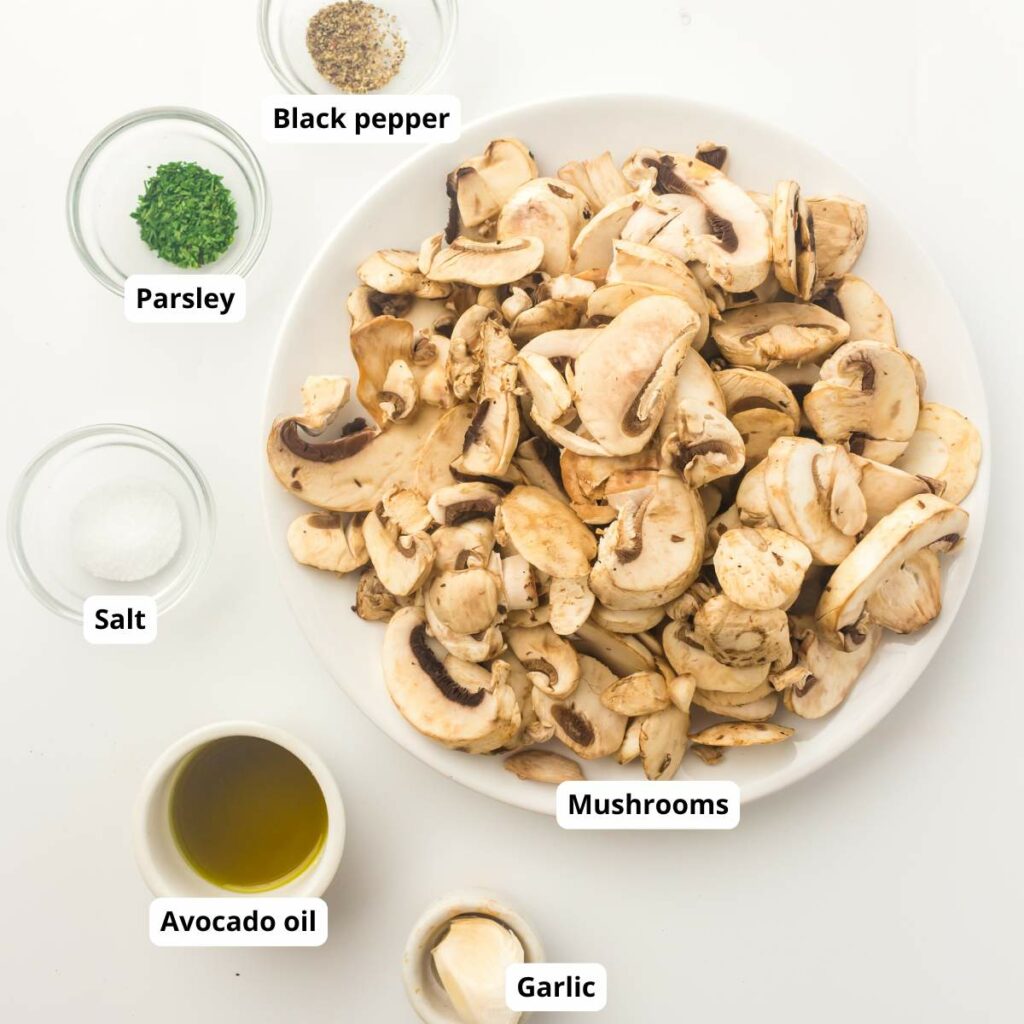 A plate of sliced mushrooms surrounded by labeled bowls of black pepper, parsley, salt, avocado oil, and garlic.