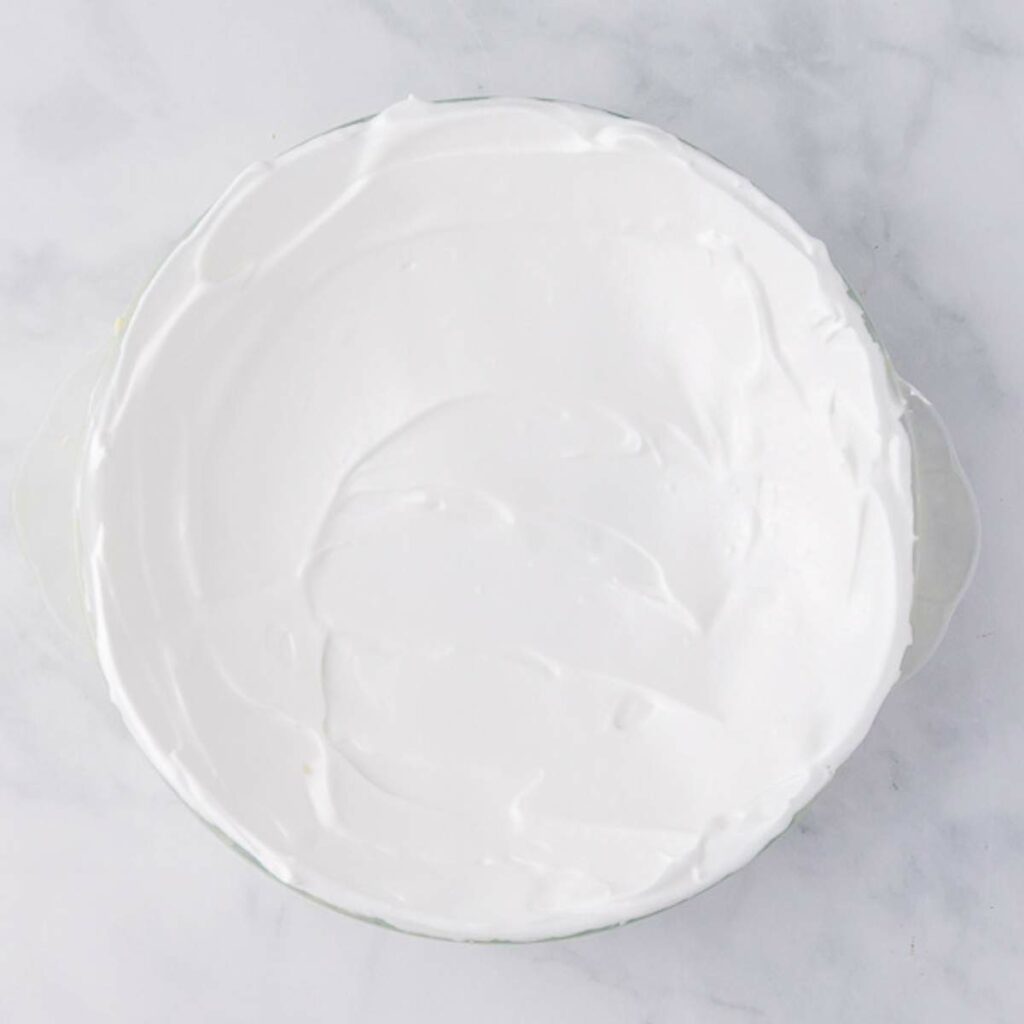 A glass dish filled with a smooth layer of white whipped topping, viewed from above on a light marble surface.