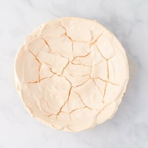A round, cracked meringue shell sits on a white marble surface.