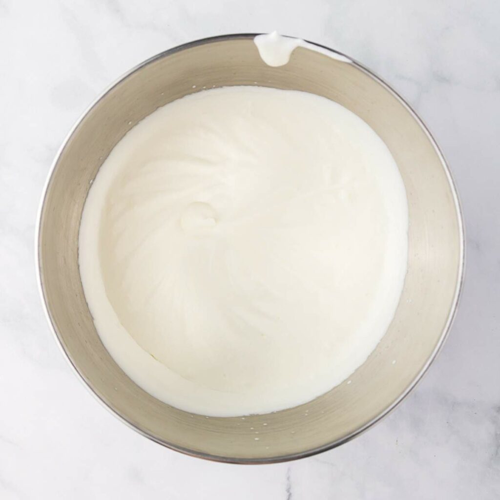 A metal mixing bowl filled with whipped cream on a white marble surface.