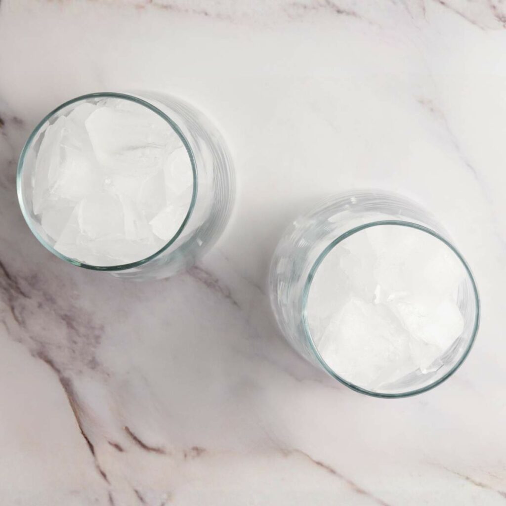Two clear glasses filled with ice cubes are placed on a white marble surface.