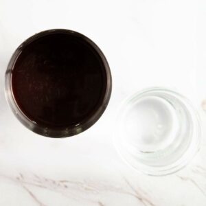 Top-down view of a glass filled with a dark liquid next to an empty clear glass on a white surface.