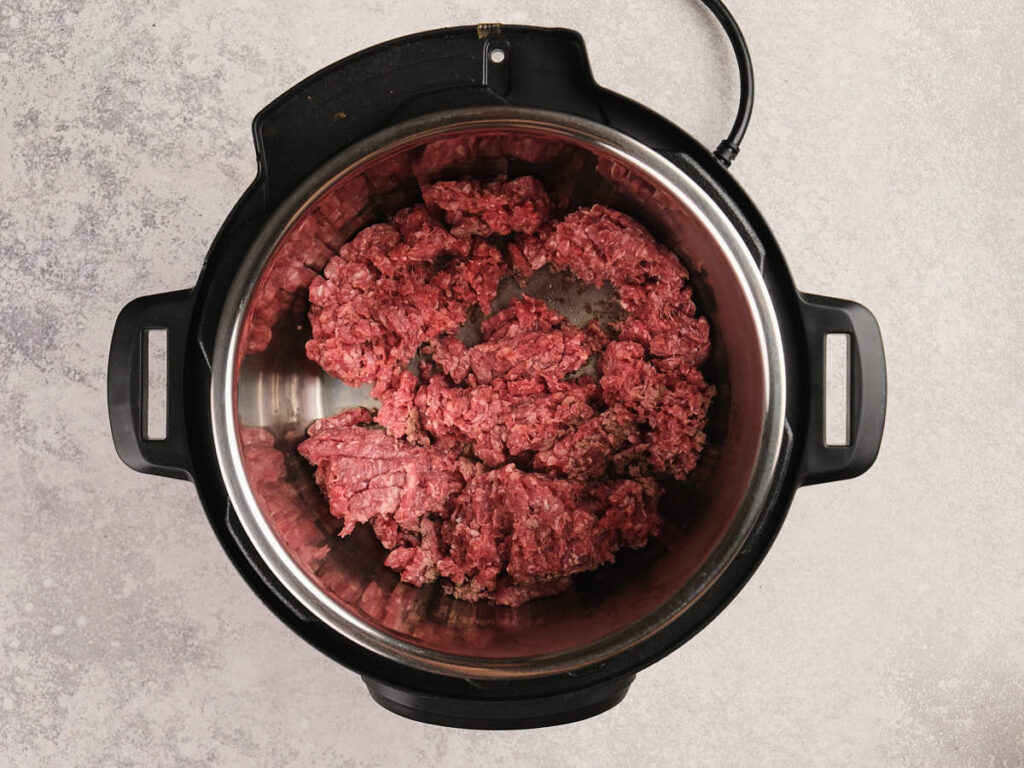 Ground beef in an electric pressure cooker, shown from above on a light countertop.