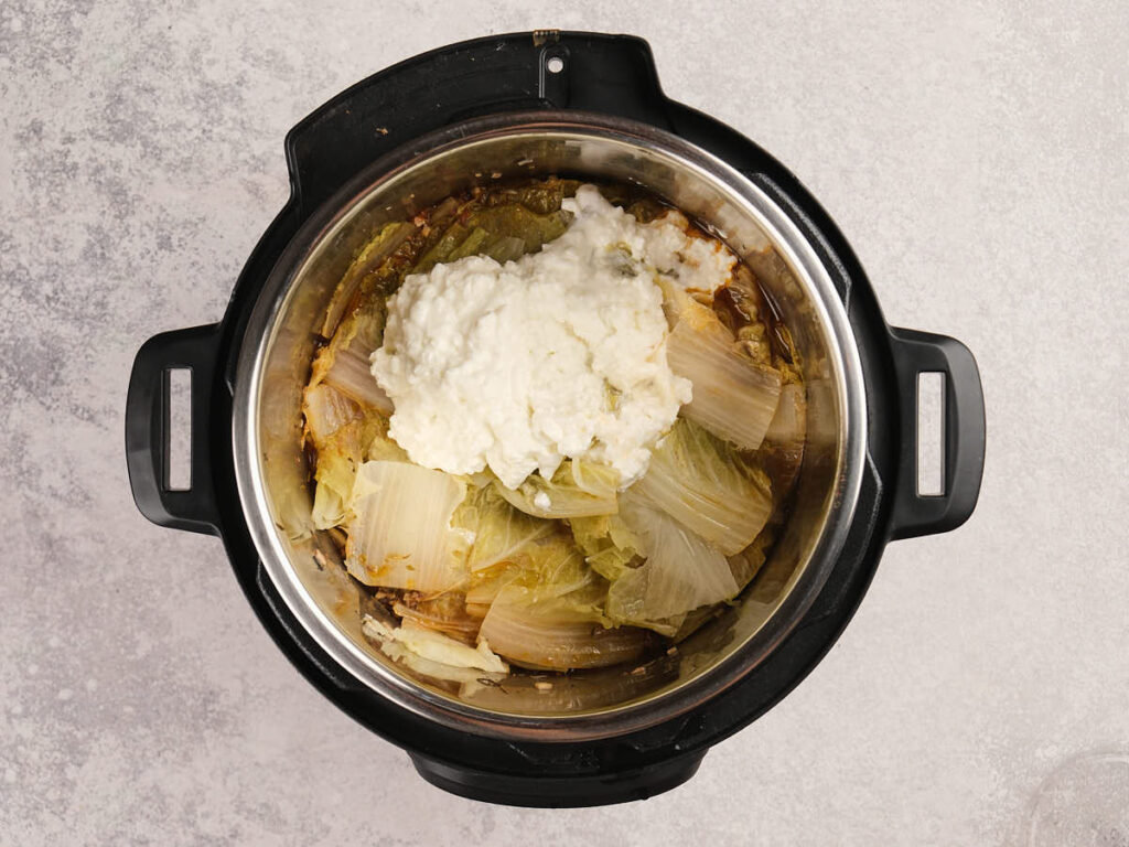 An overhead view of an Instant Pot containing cooked cabbage and a mound of white mixture.