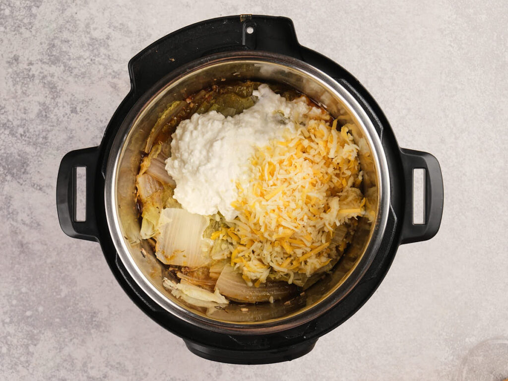 An overhead view of an Instant Pot containing cooked cabbage, onions, shredded cheese, and cottage cheese on a light countertop.