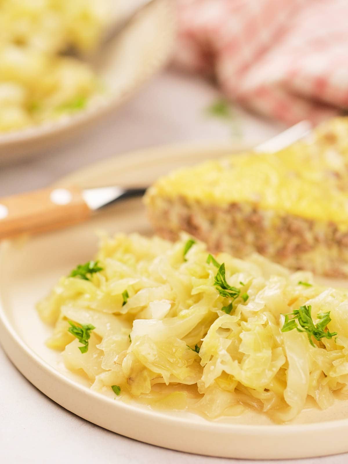 A plate with cooked cabbage garnished with parsley, served next to a slice of savory pie.