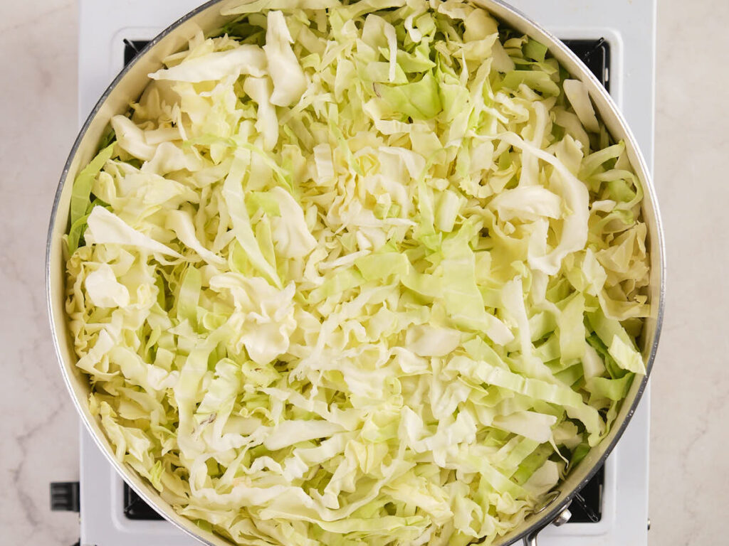 A pot filled with shredded raw cabbage sits on a stovetop burner.