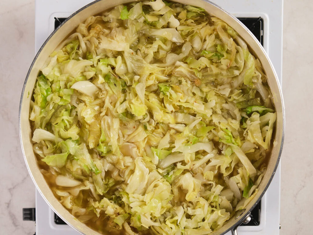 A pot of cooked cabbage sits on a stovetop, with chopped cabbage pieces simmering in liquid.