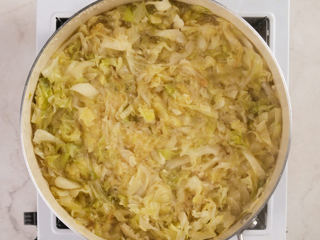 A pot filled with cooked, chopped cabbage sits on a stovetop.