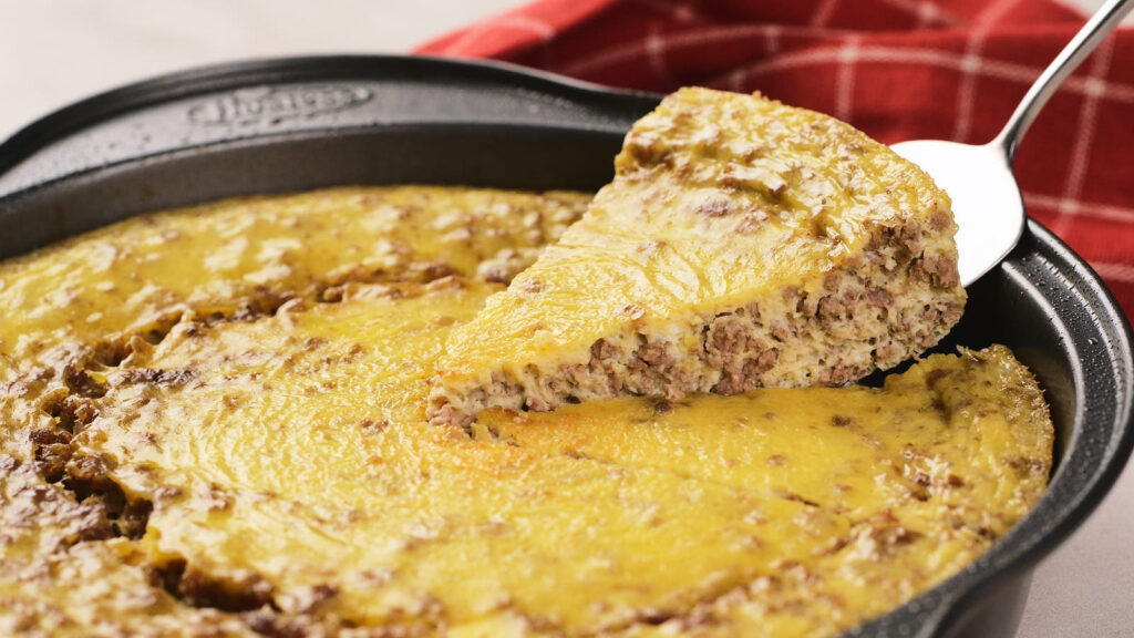 A metal pan with a baked, cheesy ground beef casserole. A serving is being lifted out with a metal spatula.