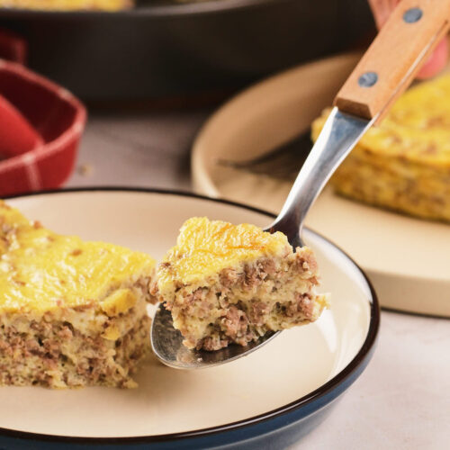 A close-up of a fork holding a bite of a baked casserole with ground meat and egg.