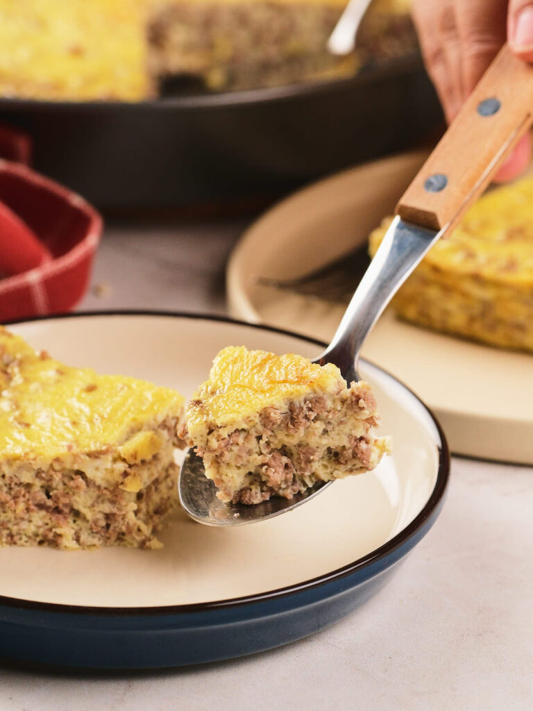 A close-up of a fork holding a bite of a baked casserole with ground meat and egg.