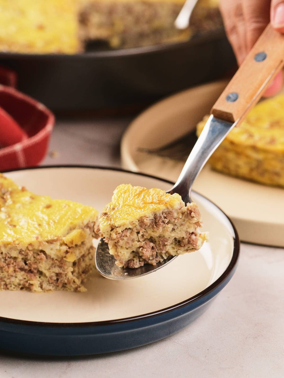 A close-up of a fork holding a bite of a baked casserole with ground meat and egg.