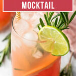 A glass of sparkling grapefruit mocktail with ice, a lime slice, and rosemary garnish on a light surface.