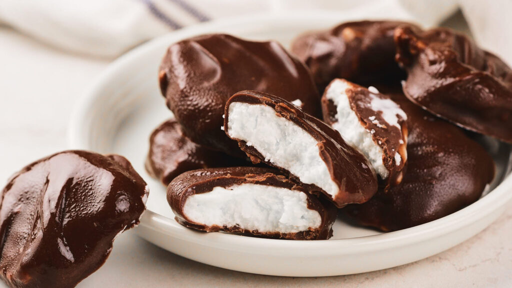A plate of chocolate-covered candies with a white, creamy filling, some whole and some split open to show the inside.