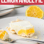 A slice of lemon angel pie with a meringue crust and creamy topping on a white plate, with a fork and a halved lemon in the background.
