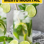 A glass of mint and lime mojito mocktail with ice, lime slices, and mint leaves, placed on a white surface with more lime and mint nearby.