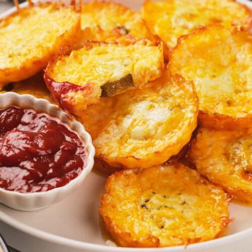 A plate of baked pickle chips with a side of ketchup in a small dish.