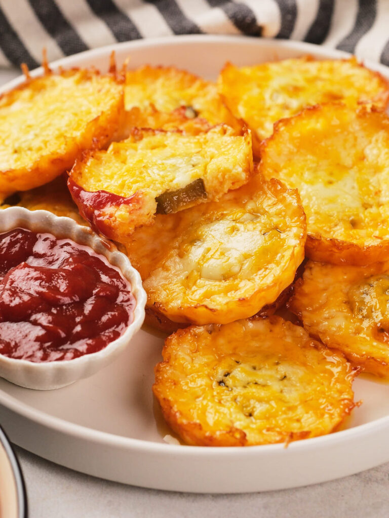 A plate of baked pickle chips with a side of ketchup in a small dish.