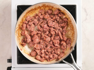 A frying pan filled with browned ground meat sits on a white stovetop.
