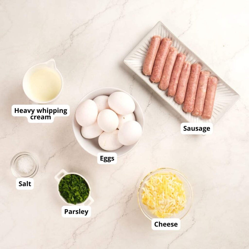 Bowls of eggs, grated cheese, chopped parsley, sausage links, salt, and a cup of heavy whipping cream.