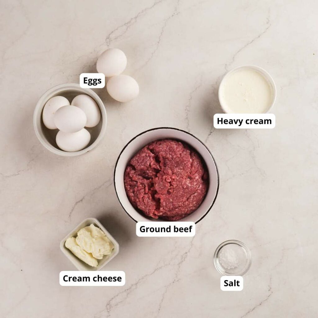 Five labeled ingredients—eggs, heavy cream, ground beef, cream cheese, and salt—are arranged on a light countertop.