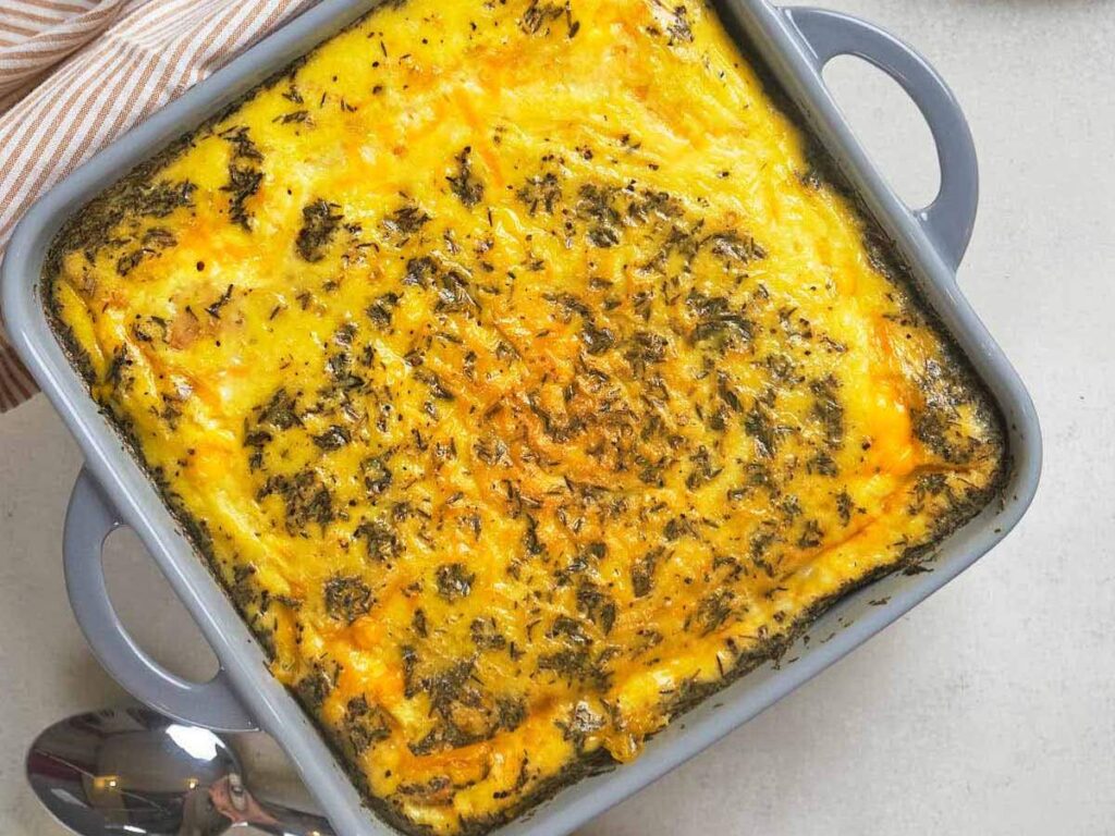 Breakfast casserole with a golden, cheesy top and sprinkled herbs in a square gray baking dish.
