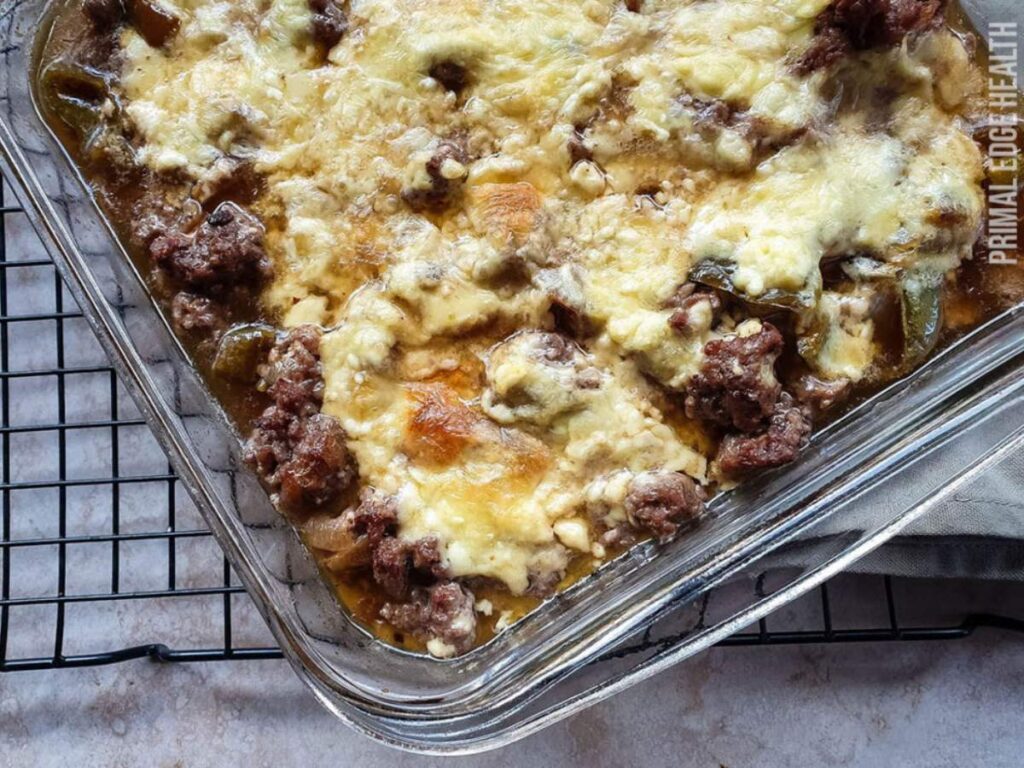 A glass baking dish filled with philly cheesesteak featuring melted cheese and browned ground meat.