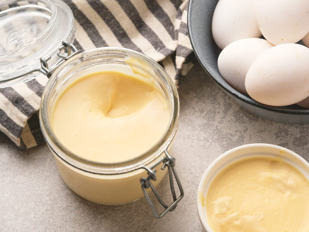A glass jar of egg pudding sits next to a striped cloth and a black bowl holding white eggs.