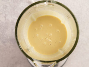 Top-down view of a blender filled with a smooth, pale yellow liquid mixture on a light countertop.